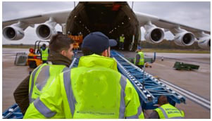 Crew members watch cargo going up into a cargo hold on a plane.